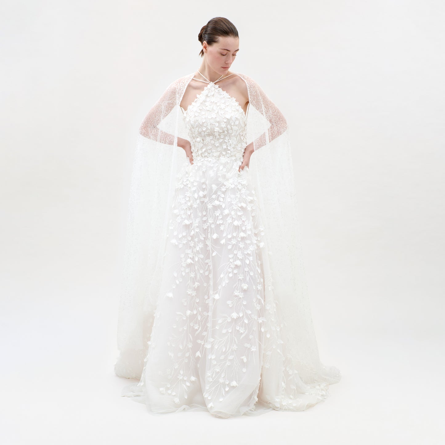 Woman wearing a white wedding dress with sheer sleeves on a light gray background