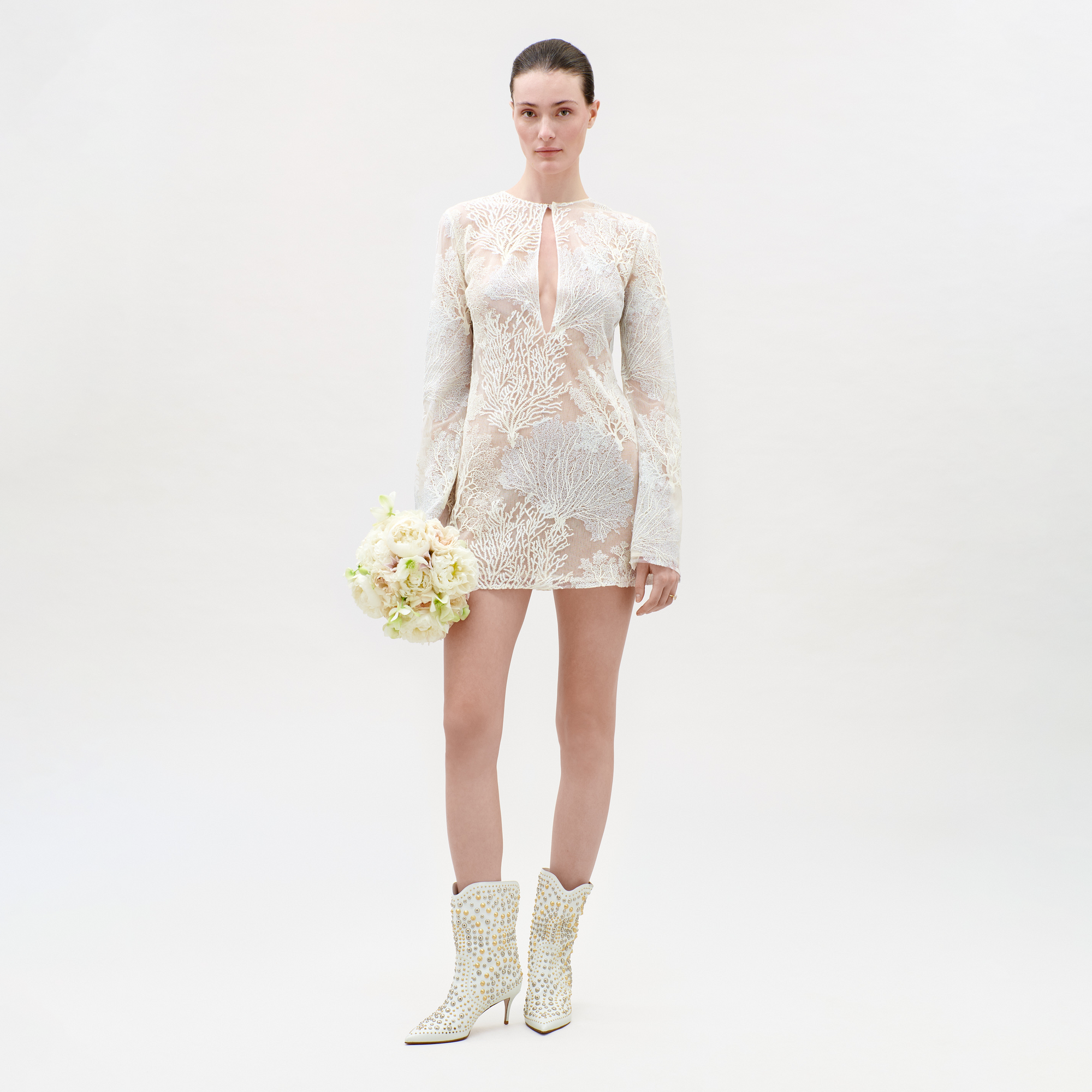 Woman wearing a white lace dress and matching boots on a plain background