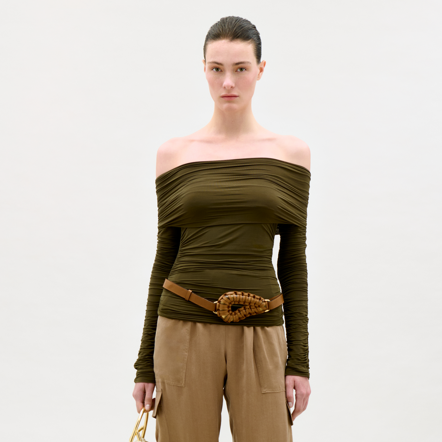 Woman wearing an off-shoulder green top and beige pants on a white background