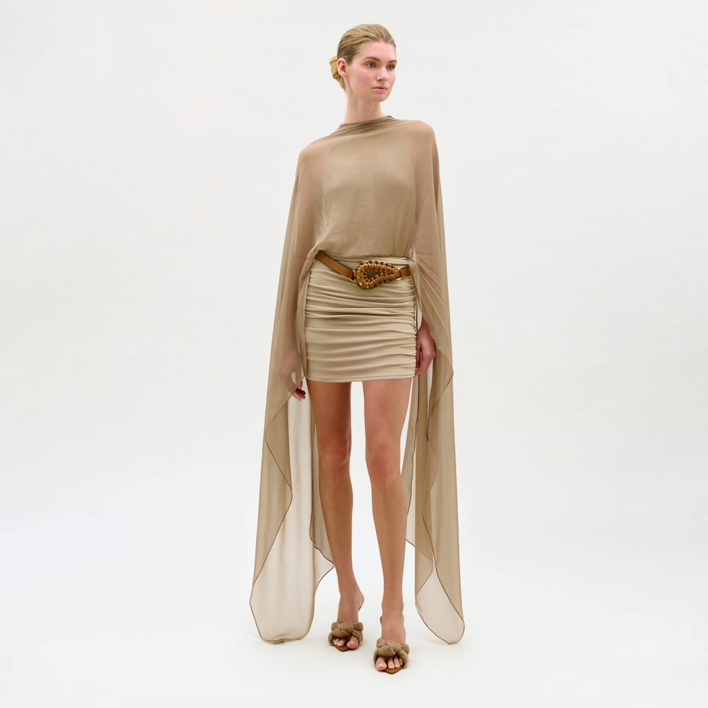 Woman wearing a beige outfit with a cape on a white background