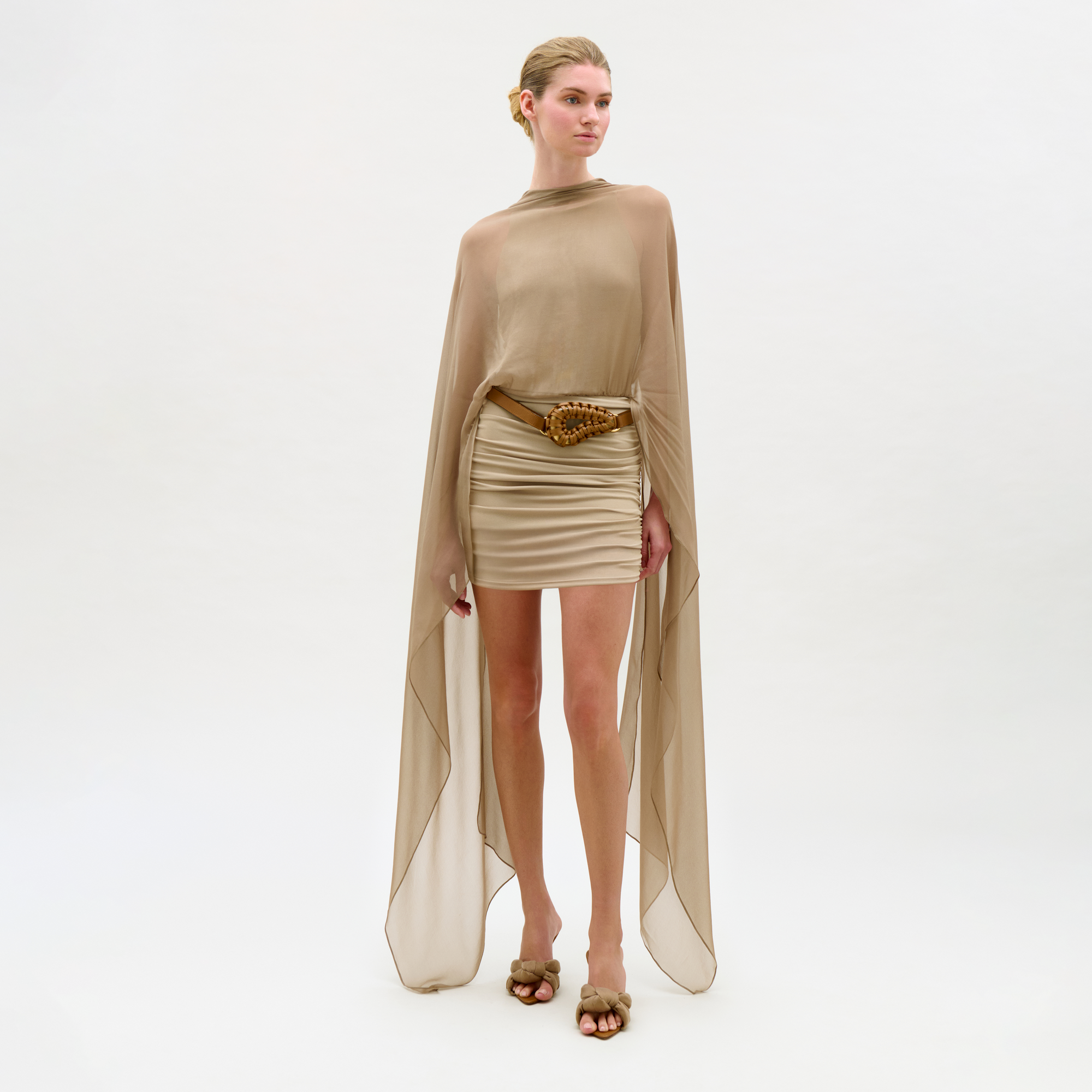 Woman wearing a beige outfit with a cape on a white background