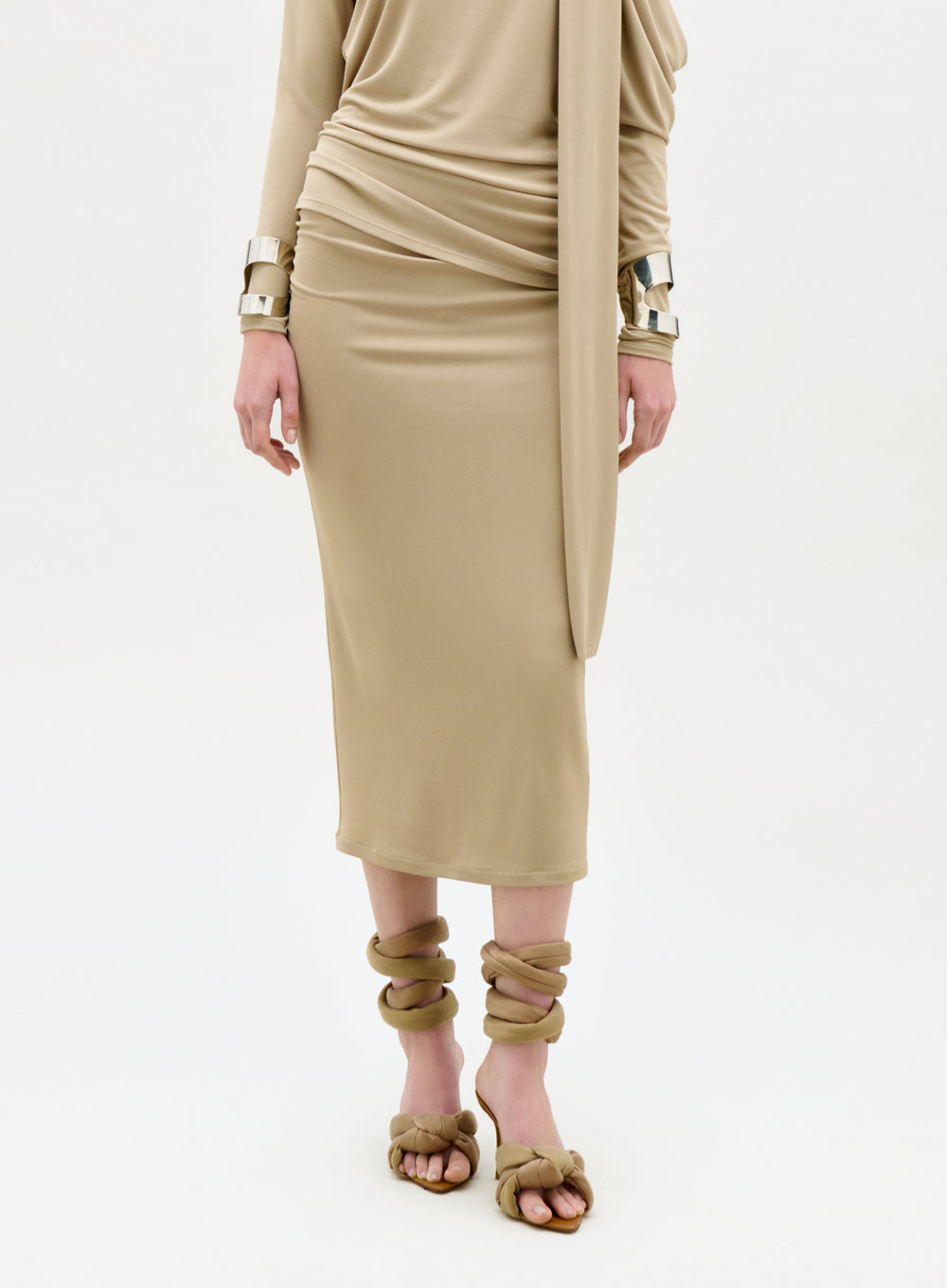 Person wearing a beige dress with gold accessories on a white background