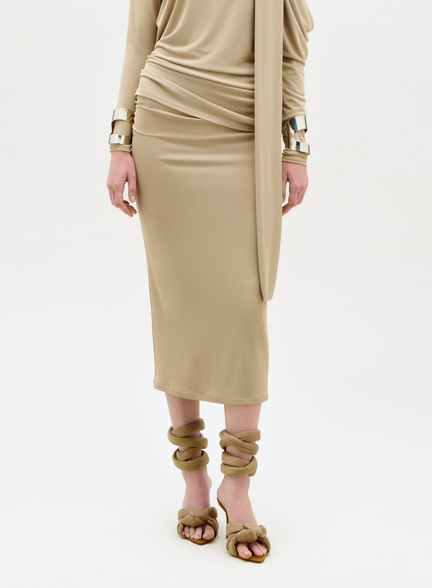 Person wearing a beige dress with gold accessories on a white background