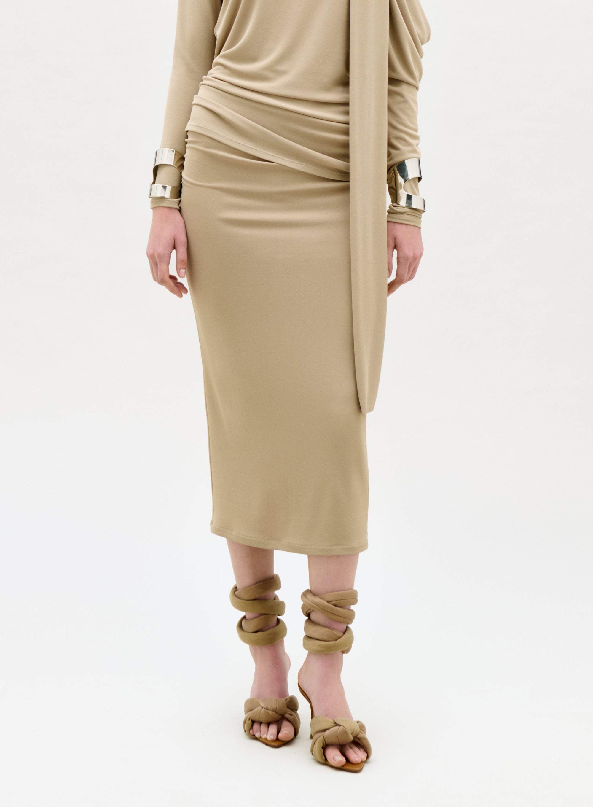 Person wearing a beige dress with gold accessories on a white background