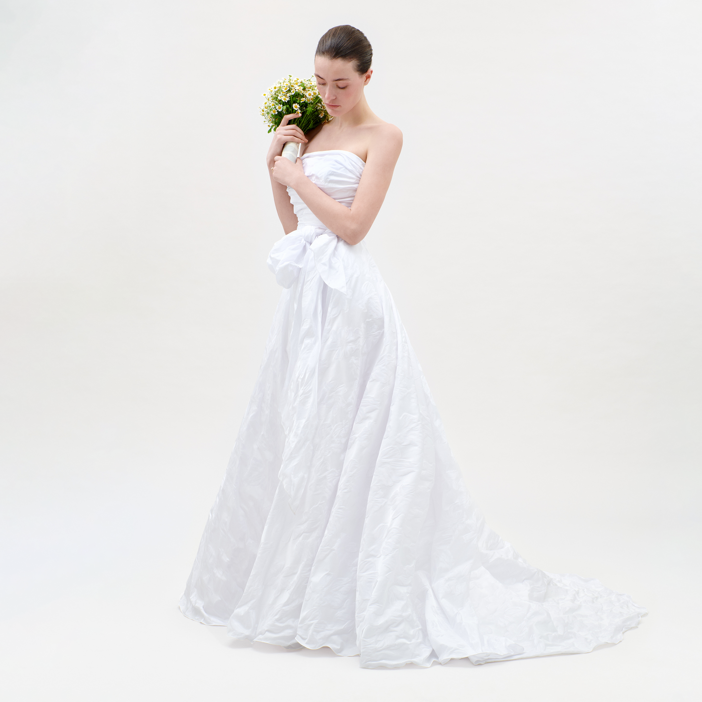 Woman in a white strapless gown holding a bouquet of flowers on a plain background