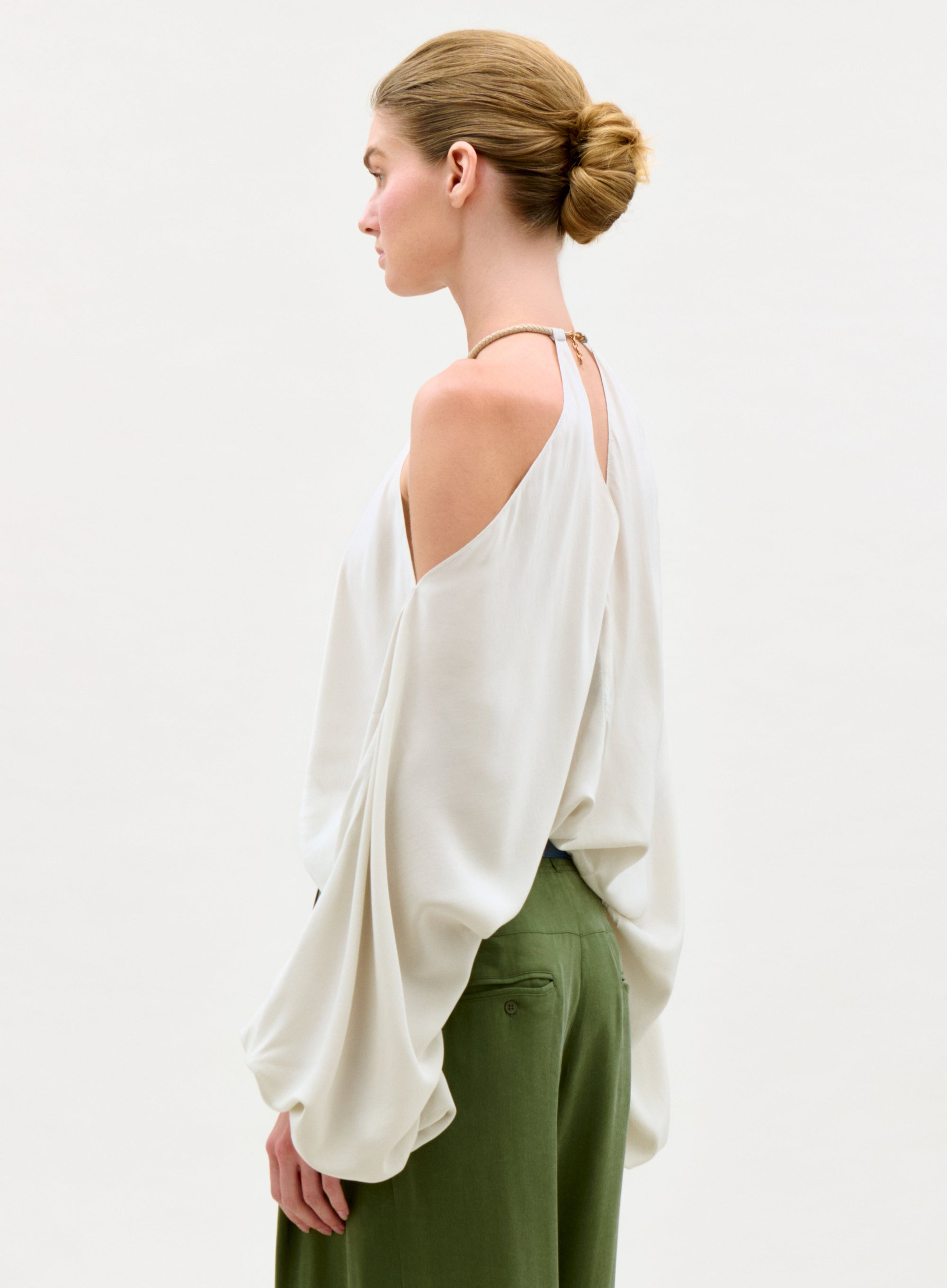 Woman wearing a white blouse with green pants on a plain background