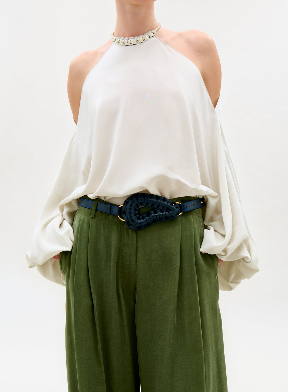 Person wearing a white blouse and green pants with a blue belt on a white background