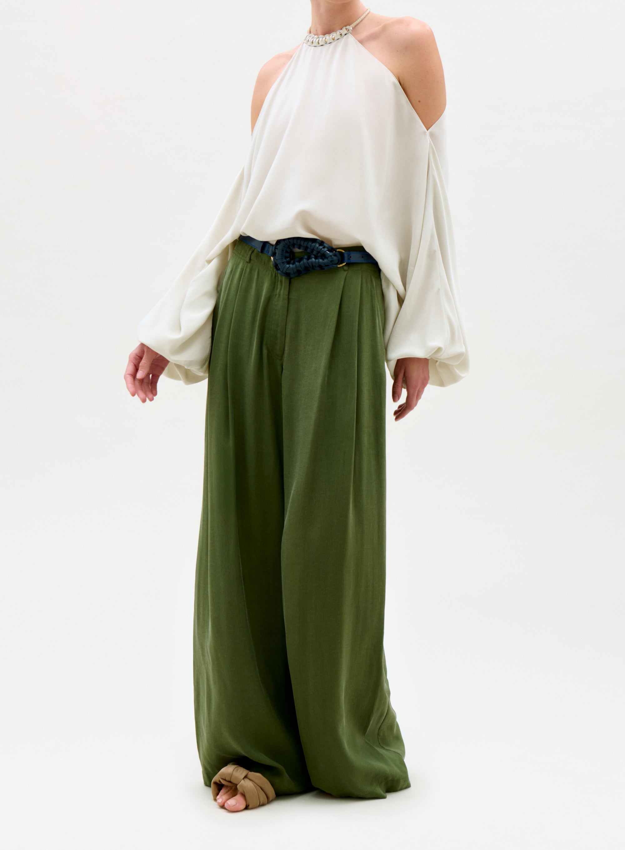 Person wearing a white off-shoulder top and green wide-leg pants on a white background