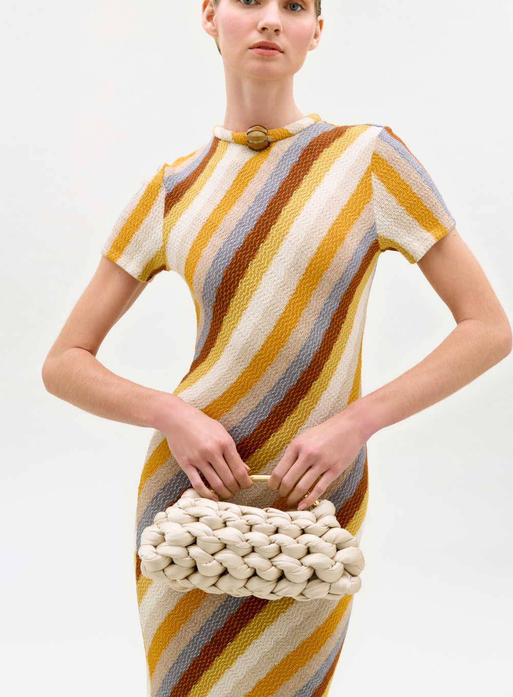 Woman wearing a striped dress holding a textured clutch against a white background