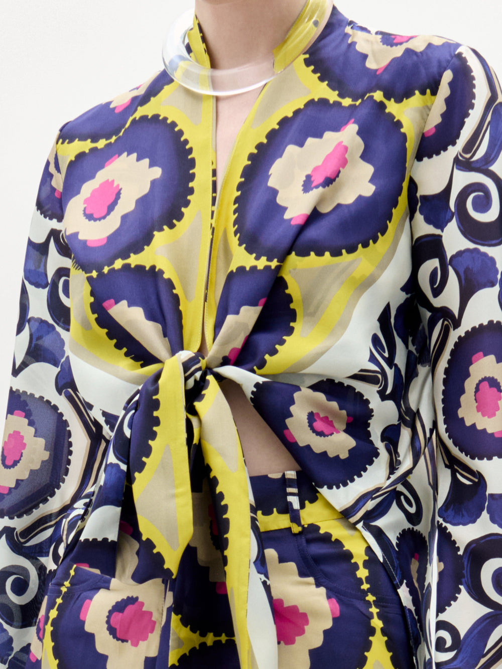 A person wears the Honey Blouse by SVT DESIGNS, a long-sleeved silk top with bold yellow, navy, cream, and magenta circles. A front twist detail reveals a hint of midriff, making the blouse pop against a plain white background.