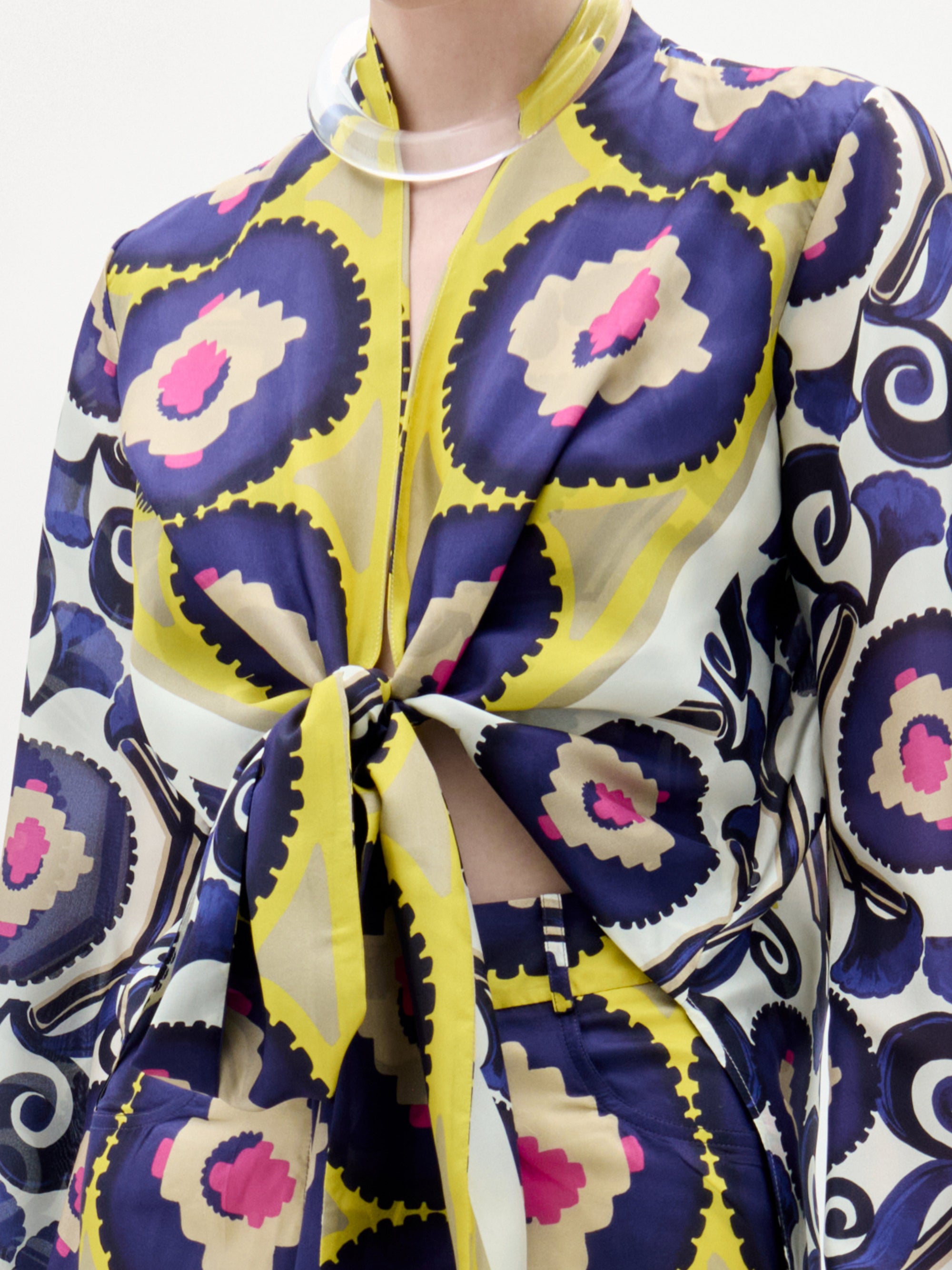 A person wears the Honey Blouse by SVT DESIGNS, a long-sleeved silk top with bold yellow, navy, cream, and magenta circles. A front twist detail reveals a hint of midriff, making the blouse pop against a plain white background.