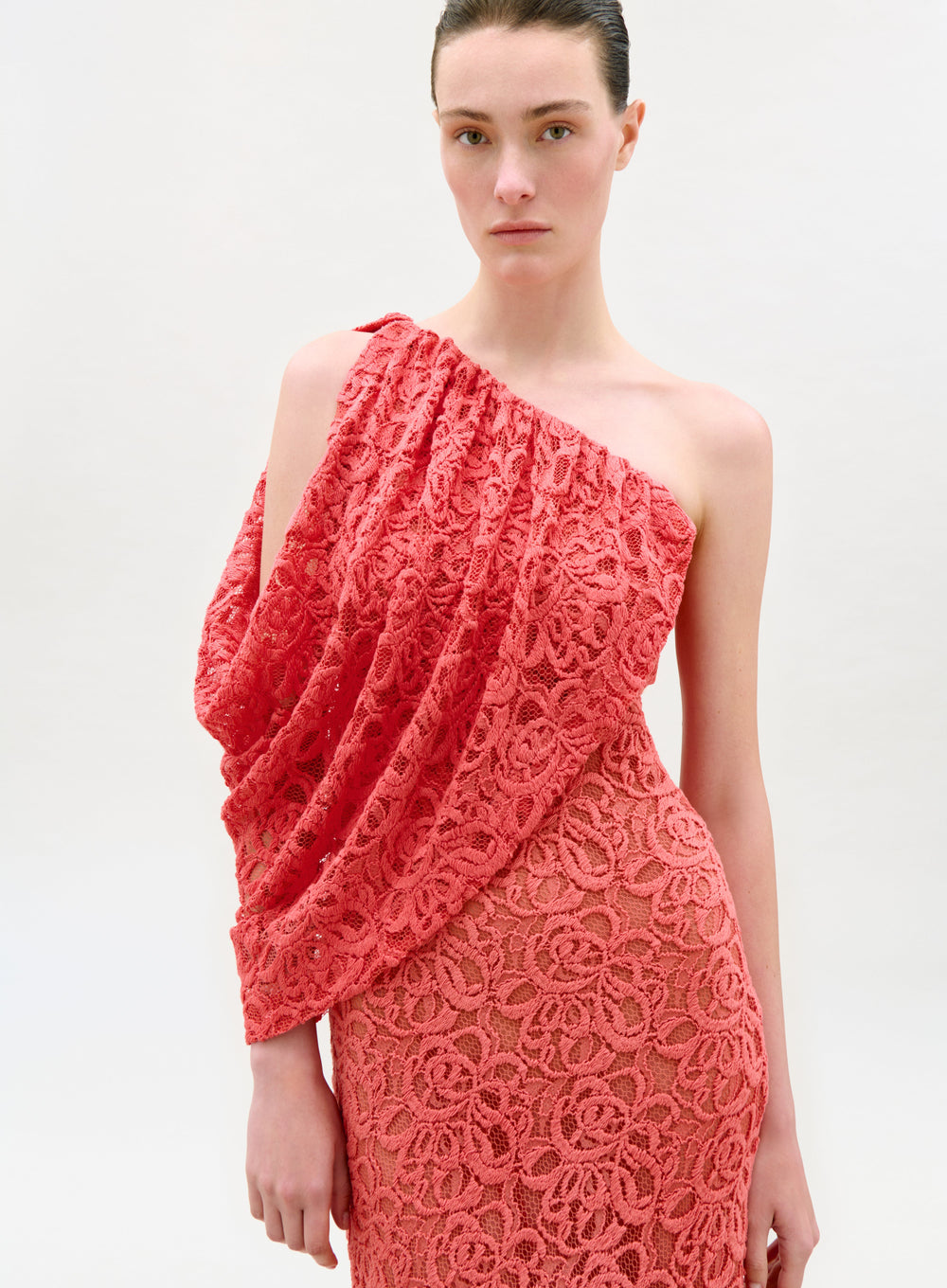 Woman wearing a coral lace one-shoulder dress on a white background