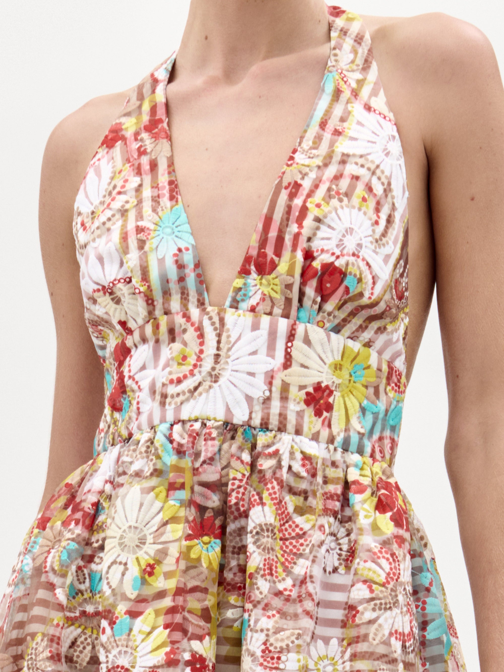 A person wearing the Kairi Dress by SVT DESIGNS—a sleeveless halter midi with a deep V-neckline and a vibrant floral and geometric pattern in red, brown, white, yellow, and blue. Only the upper torso is visible.