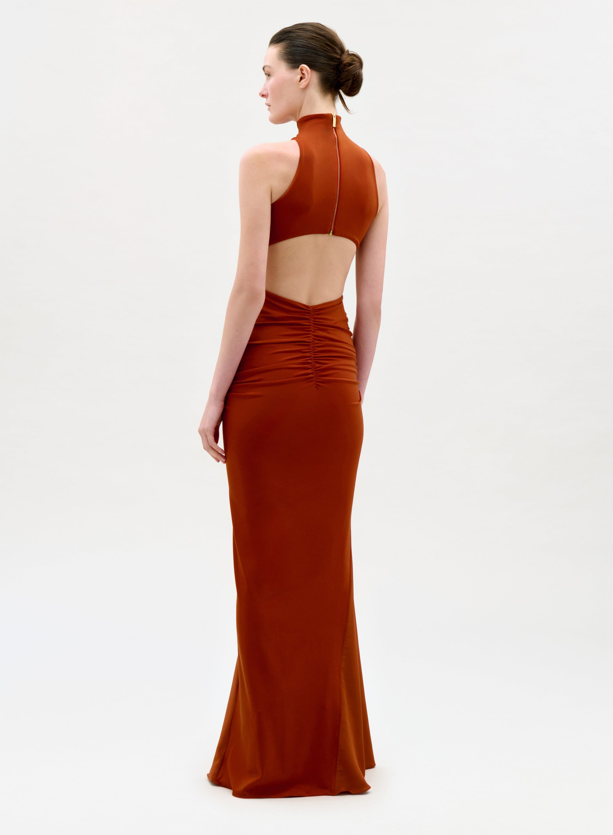 Woman wearing a rust-colored halter neck gown on a white background