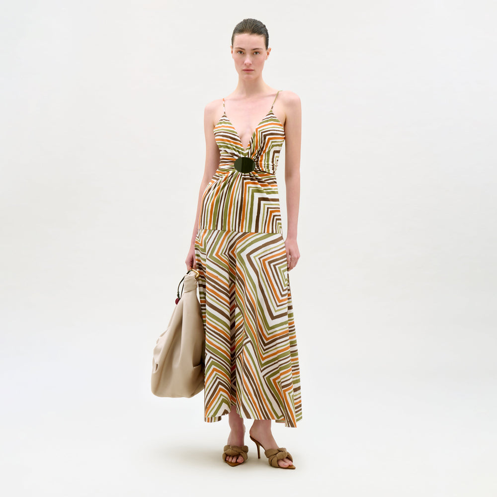 Woman wearing a patterned dress holding a beige bag on a white background