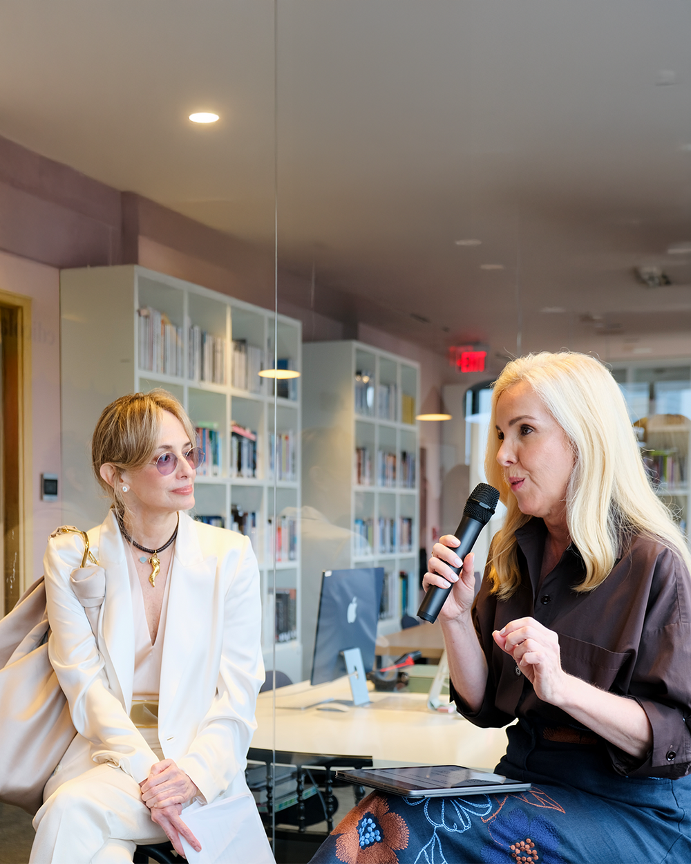 Two women in a professional setting with one holding a microphone.