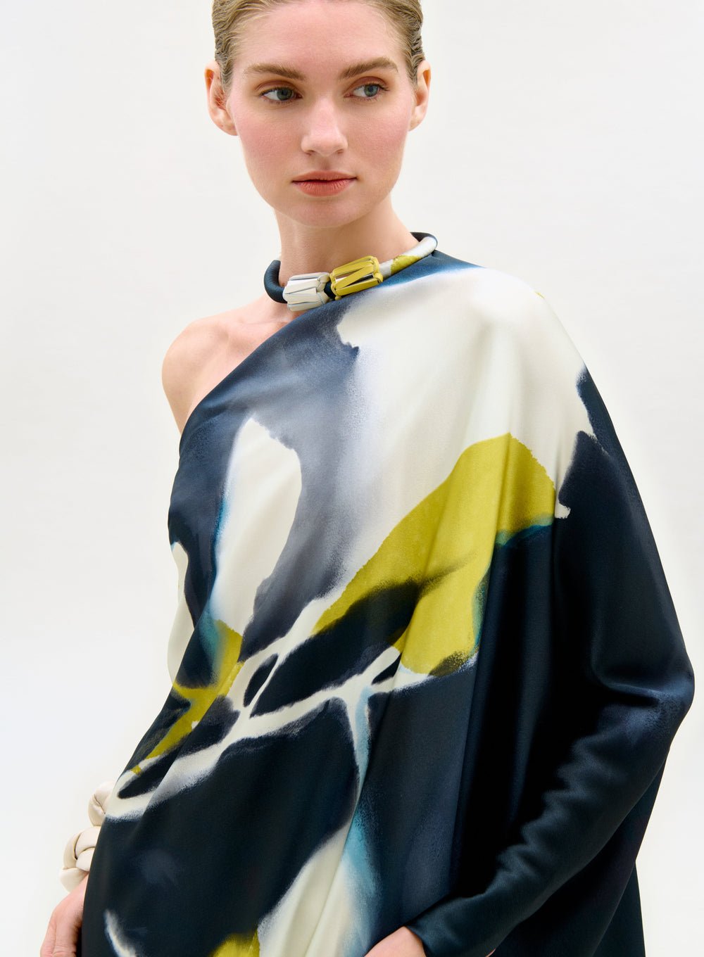 Model wearing a colorful one-shoulder top with abstract design on a plain background