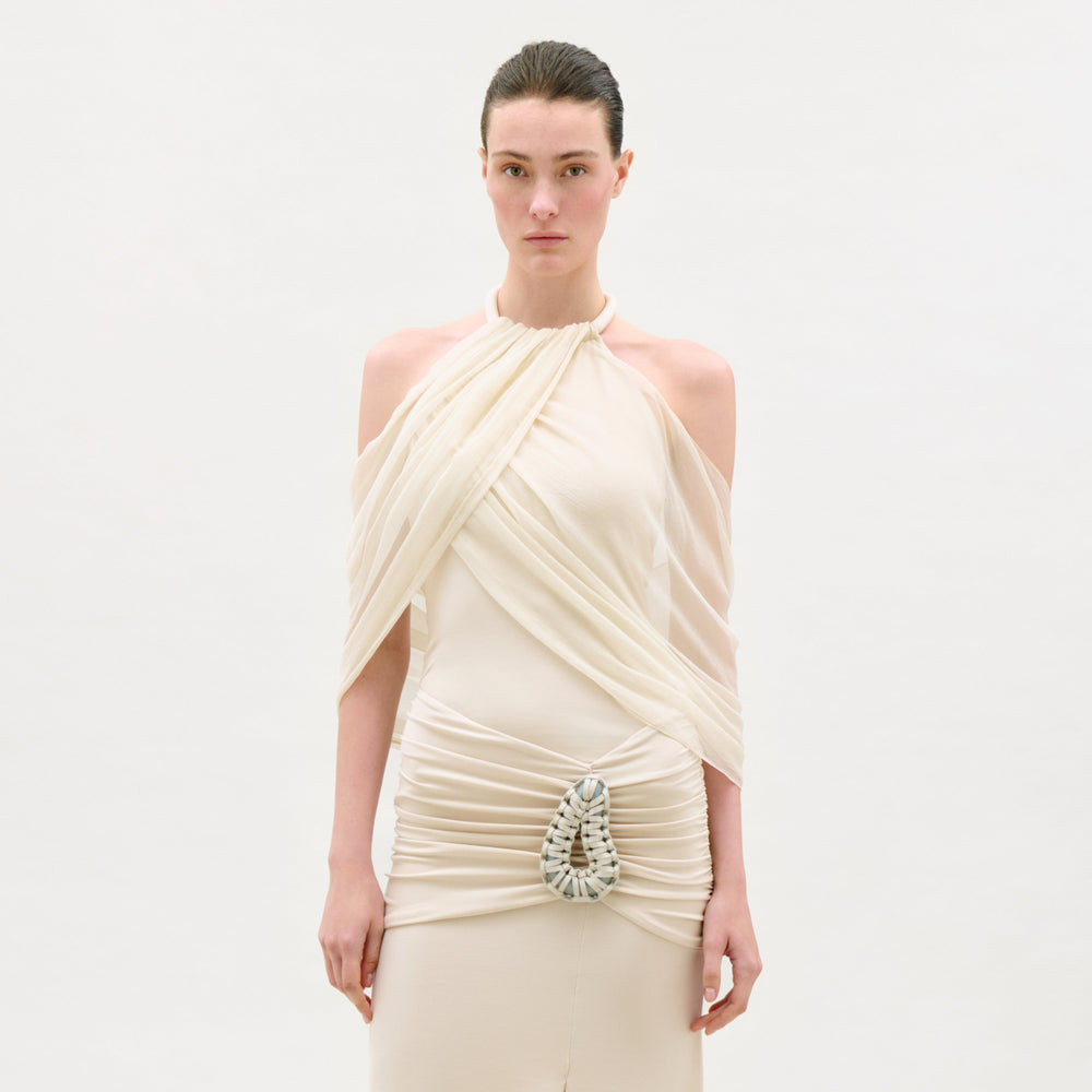 Woman wearing a beige draped dress with a decorative element on a white background