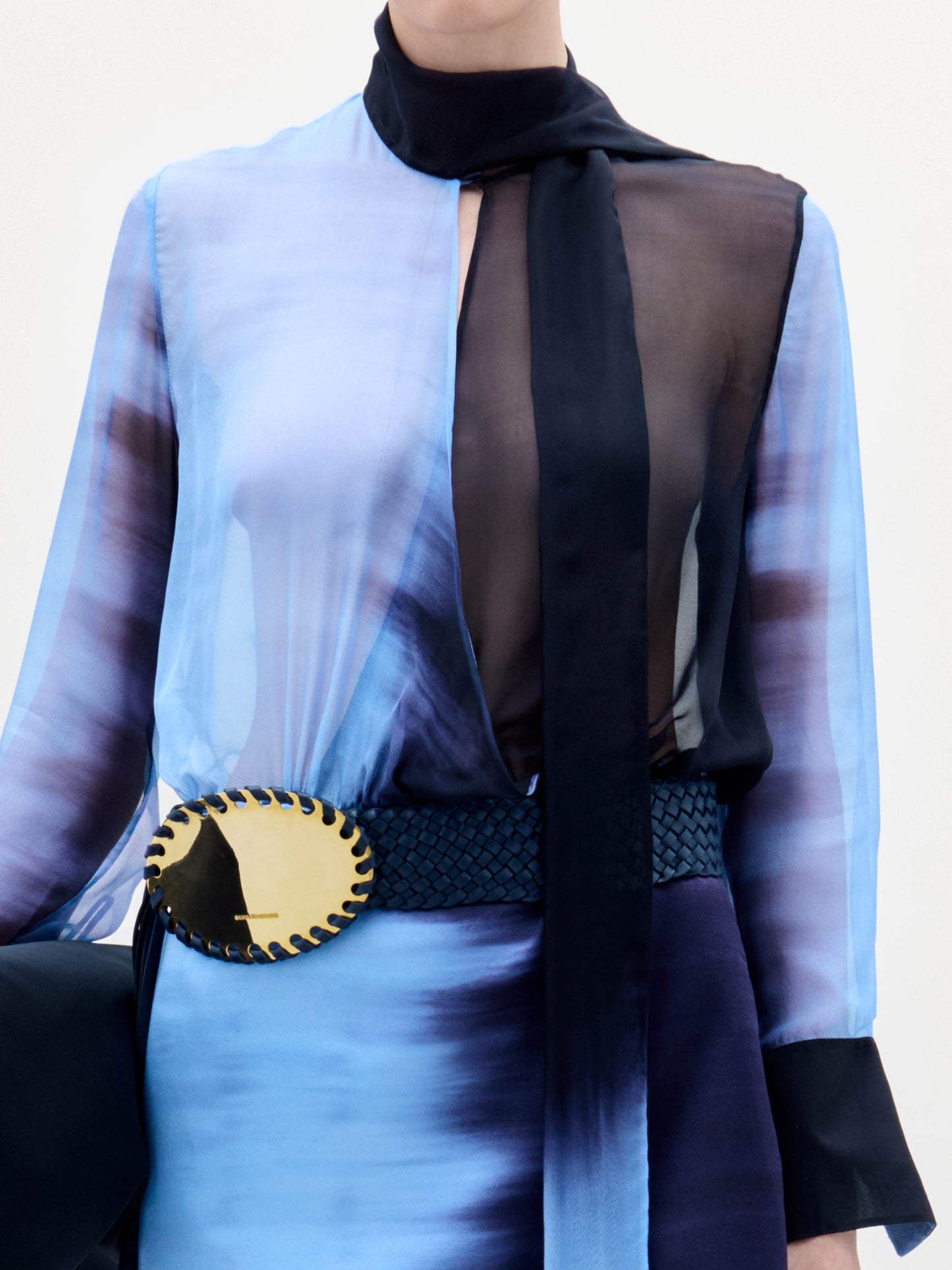A woman stands against a white background wearing the Imelda Dress, styled with black sandals, a black bag, and a belt featuring a large gold decorative buckle.