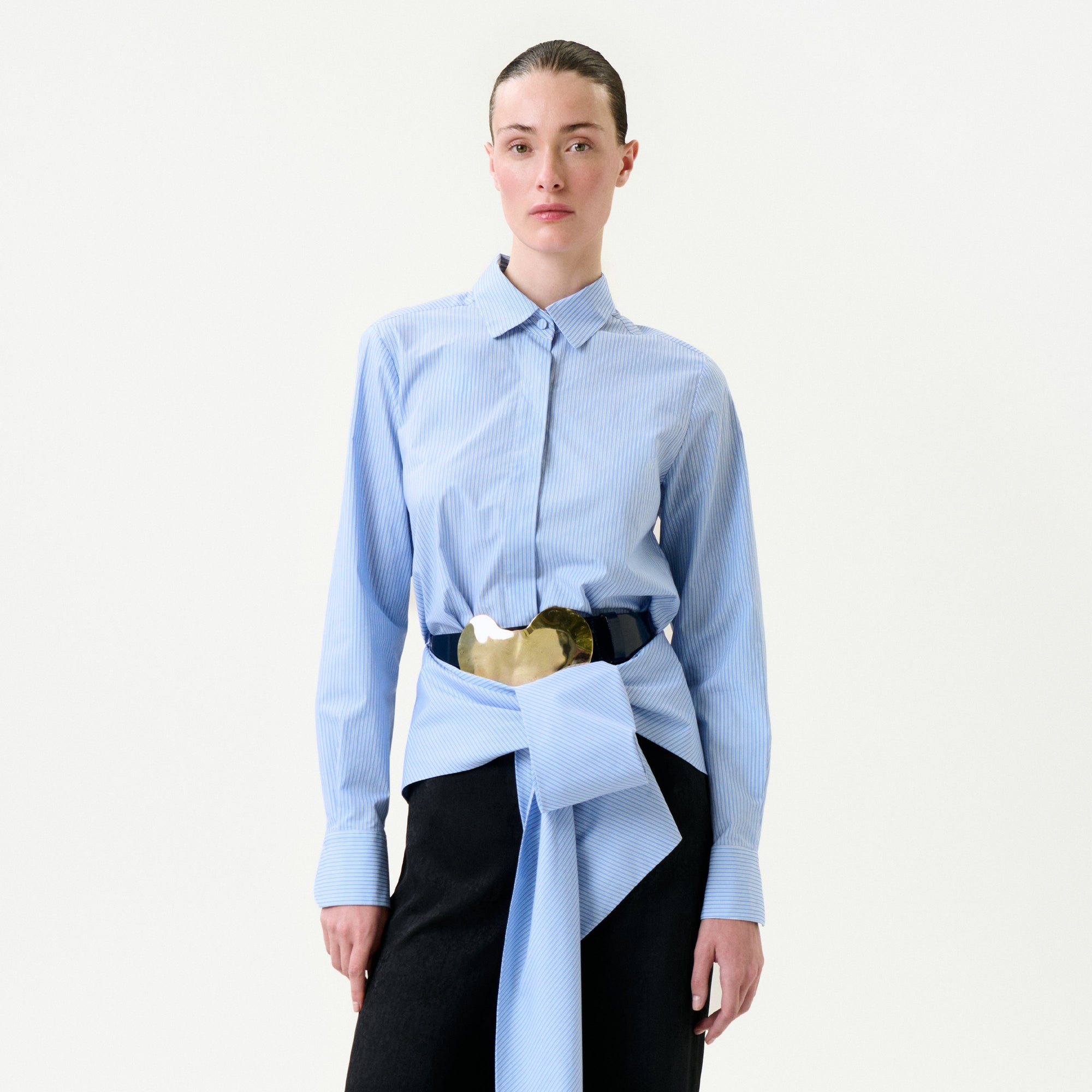 Person wearing a light blue shirt with a gold belt and black pants on a white background