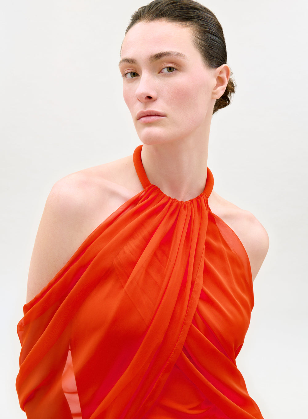 Woman wearing an orange halter neck dress against a white background