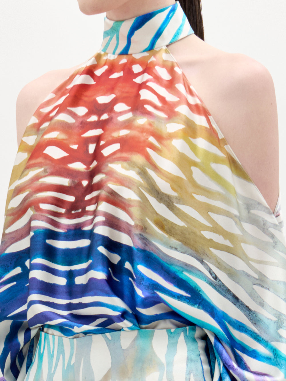 A person wearing the Safira Blouse by SVT DESIGNS, a sleeveless, high-neck top with a colorful abstract print in red, yellow, blue, and white. Only the torso and part of the face are visible.