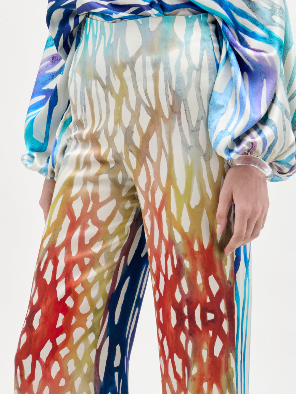 A person wearing the SVT DESIGNS Andie Pant, a high-waisted, wide-leg style with a red, yellow, and white abstract pattern, paired with a matching long-sleeved blouse; only the torso and legs are visible.