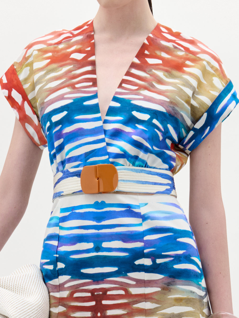 A person in the Sakura Dress by SVT DESIGNS—a short-sleeved, v-neck midi dress with a colorful stripe pattern in red, blue, white, and tan—styled with a wide beige belt and an A-line skirt.