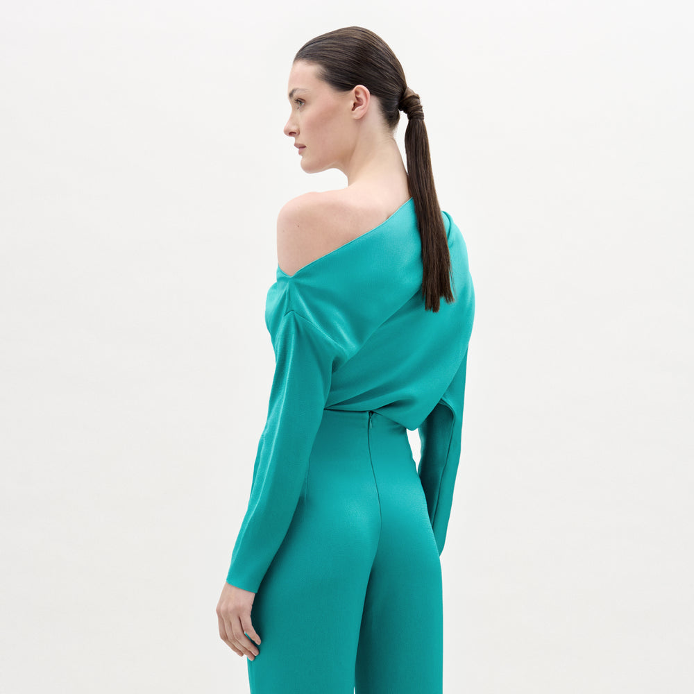 Woman wearing a teal off-shoulder jumpsuit on a light gray background
