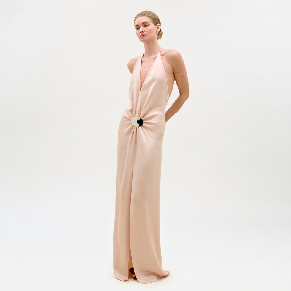 Woman wearing a long, light pink evening gown with a black detail on a white background