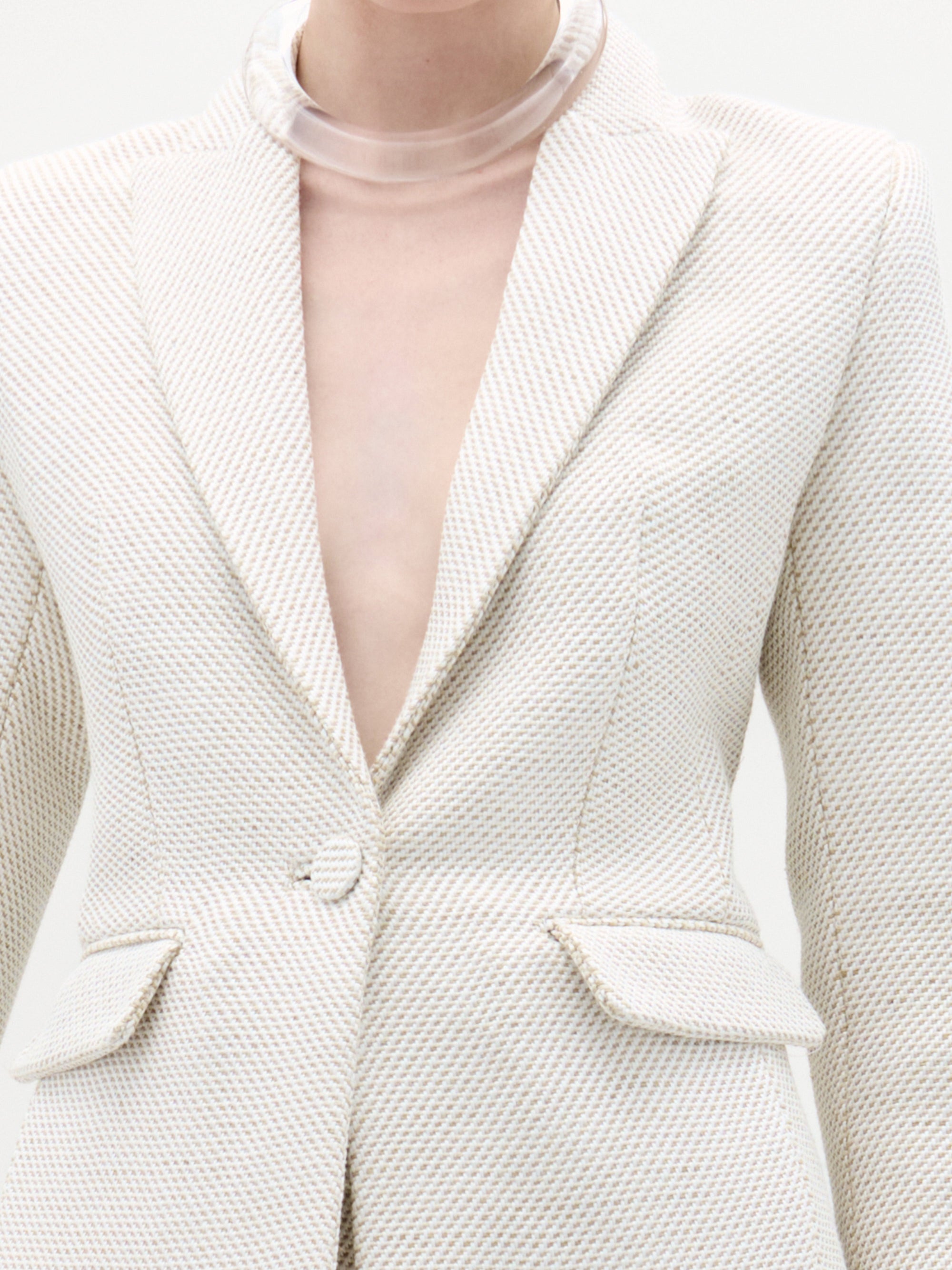 A person wears the SVT DESIGNS Rebeca Jacket, a cream-colored textured fitted blazer with single button closure and flap pockets, paired with a thick clear choker. The photo is cropped from neck to waist.