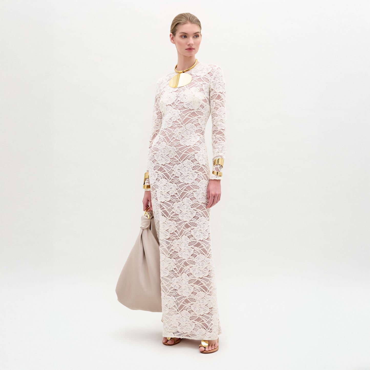 Woman wearing a long white lace dress with gold accents on a white background