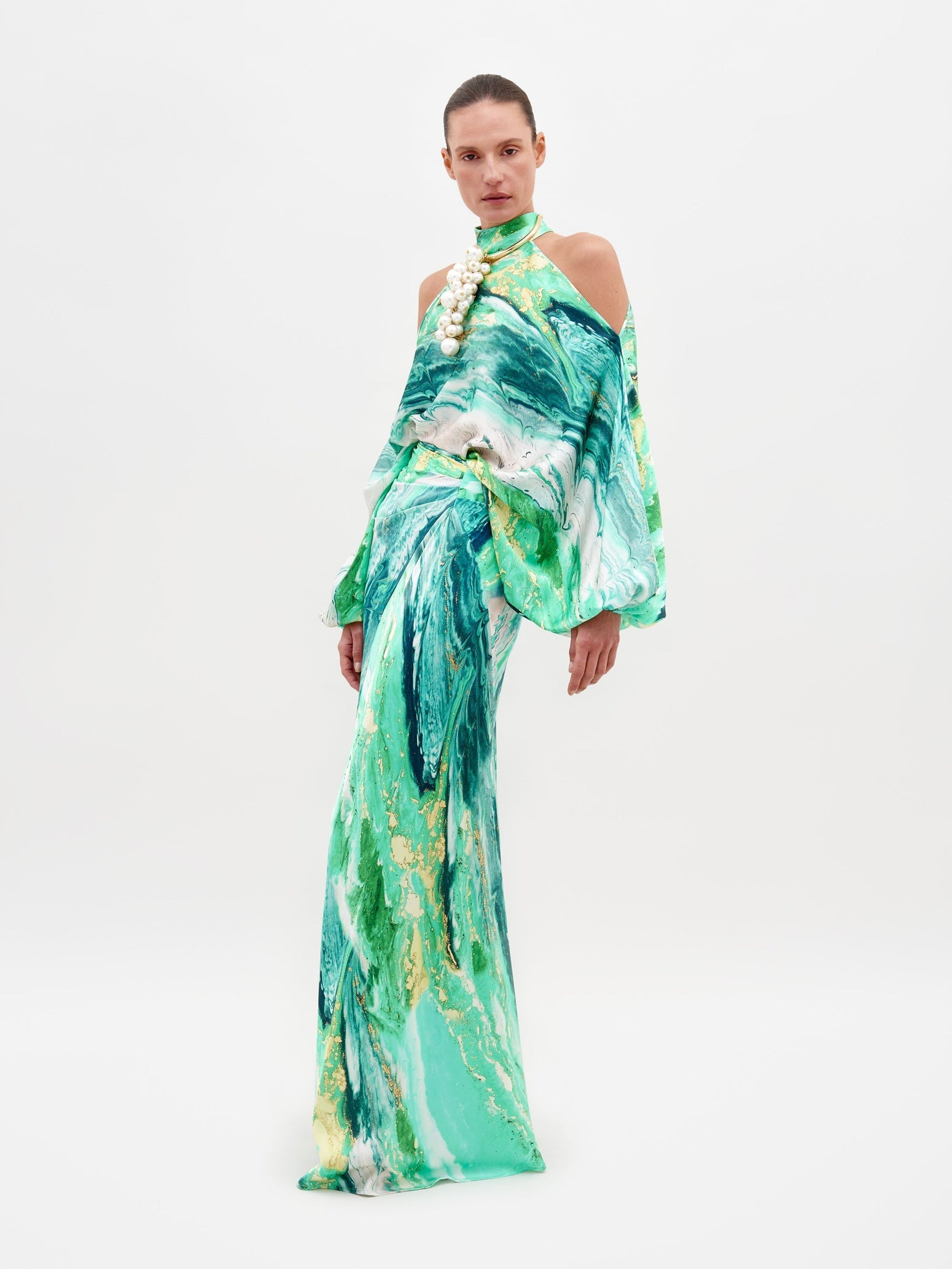 A person wearing the Claudia Skirt Green Marble dress, featuring a long-sleeved design with a shoulder cutout, poses against a plain white background. Pre-order now to ship by February 15th, 2025.