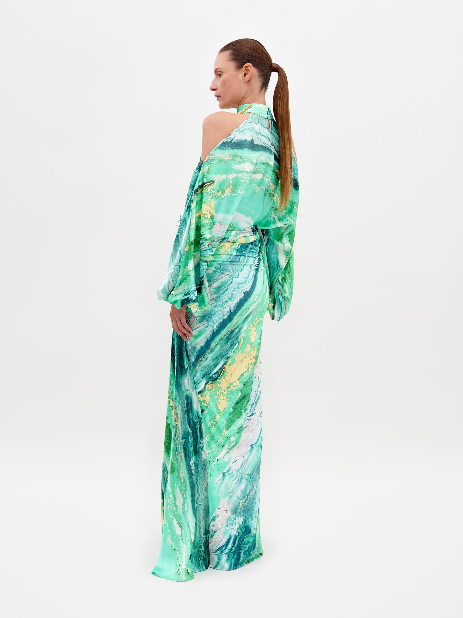 A person wearing the Claudia Skirt Green Marble dress, featuring a long-sleeved design with a shoulder cutout, poses against a plain white background. Pre-order now to ship by February 15th, 2025.