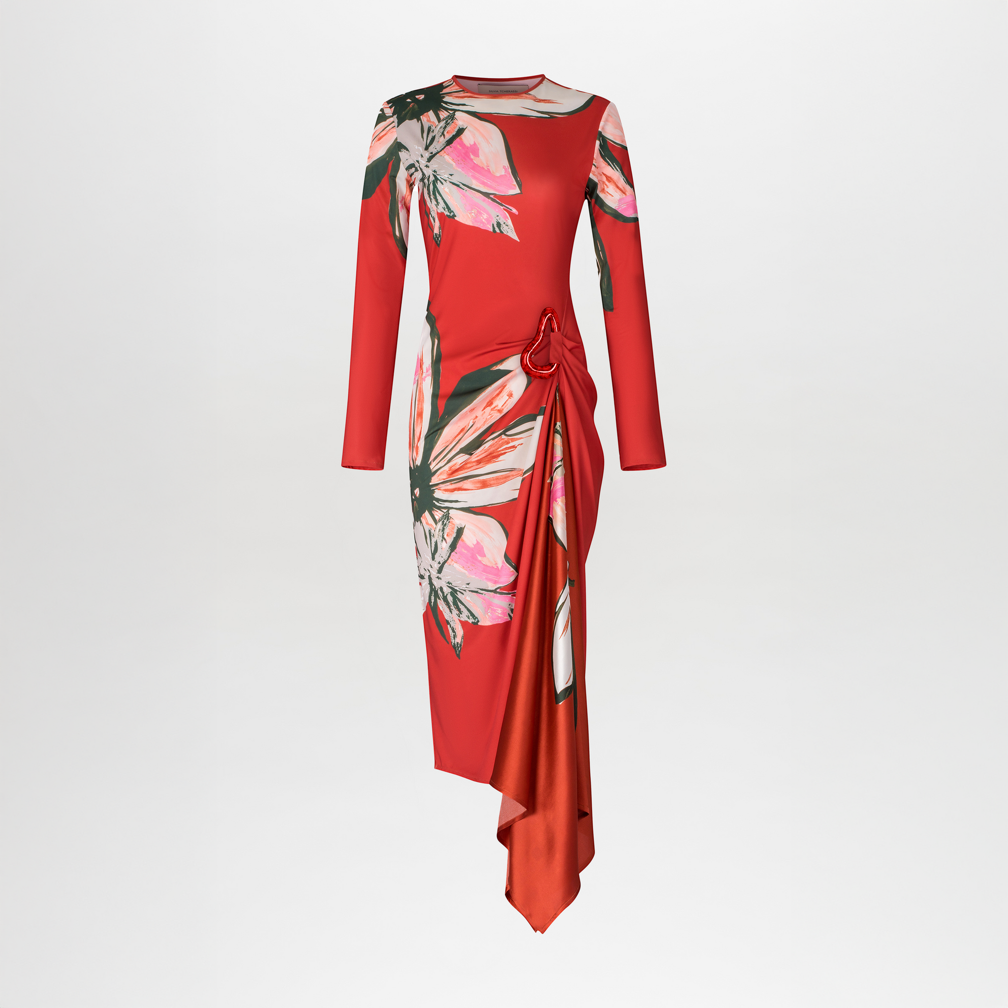 The Ananya Dress by SVT DESIGNS features long sleeves, red jersey fabric with stretch, vibrant pink and green floral prints, a fitted bodice, and an asymmetrical draped skirt. Shown on a plain white background.