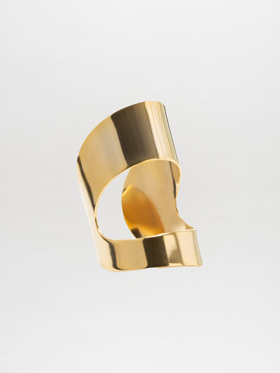 The Artemis Cuff by SVT DESIGNS is a shiny, abstract sculpture made from gold-plated brass. Its smooth, curved surfaces and spiraled design create a reflective finish that captures soft lighting against a plain white background.