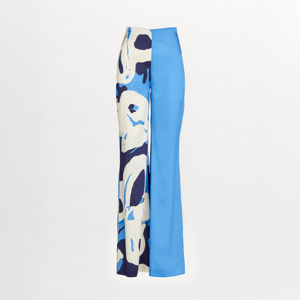 The Andie Pant by Silvia Tcherassi features a high-waisted, wide-leg silhouette with an asymmetrical design: one leg in abstract blue, white, and navy print, the other in solid bright blue. Displayed on a white background.