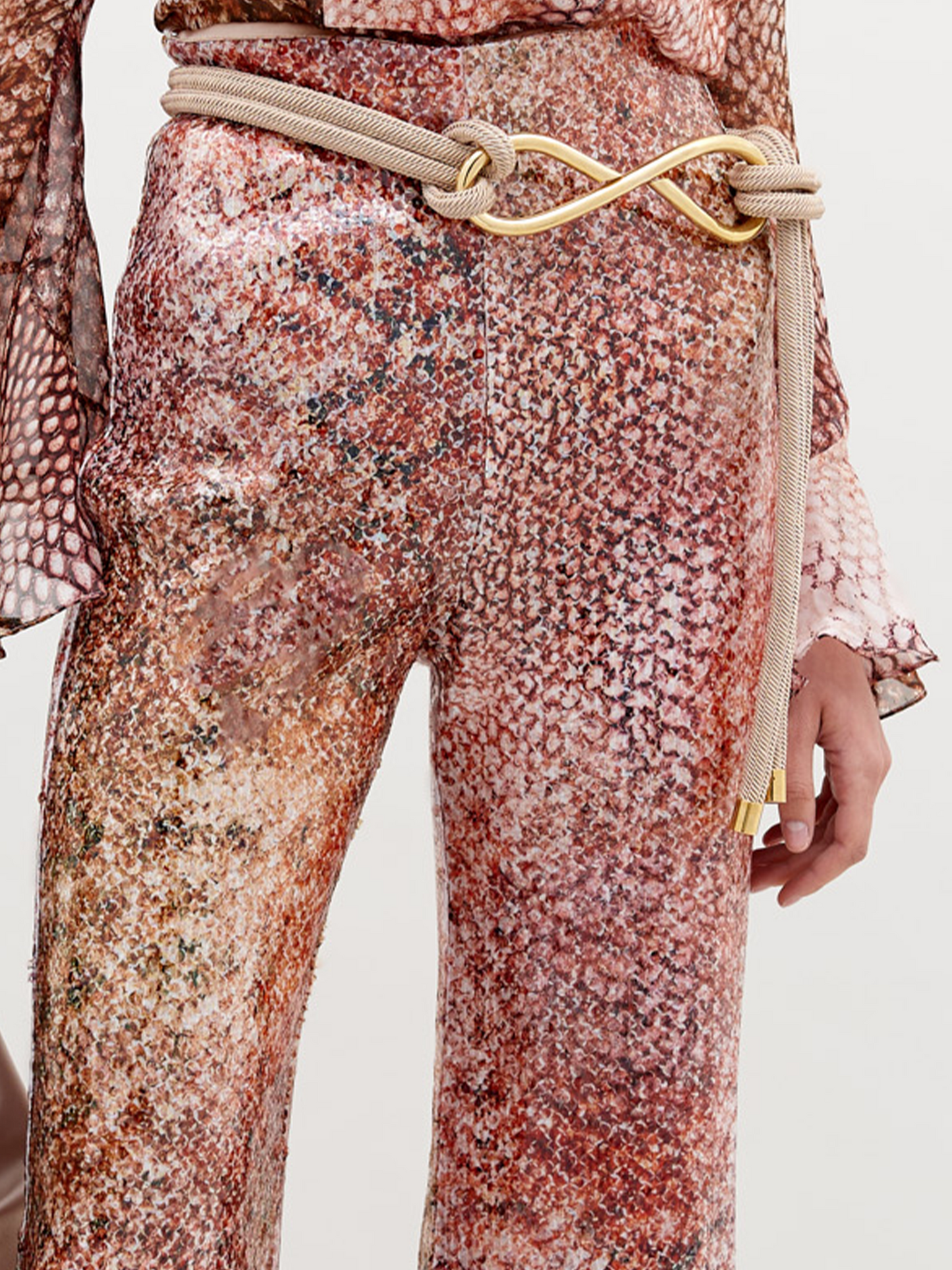 Person wearing a long-sleeved, patterned top and matching Avellino Pant Peach Animal Print with a cinched waist, holding a large beige bag in a white studio setting. Pre-order now to ensure delivery by the ship by date of November 15th, 2024.