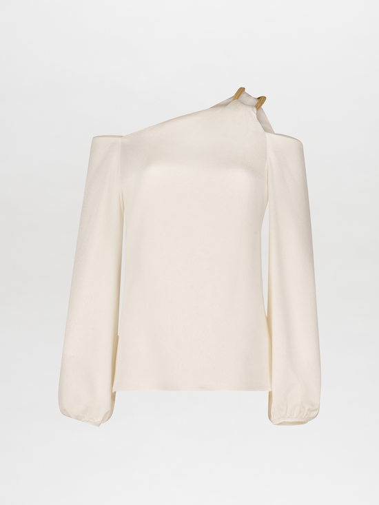 The Barb Blouse by Silvia Tcherassi US is a cream-colored, one-shoulder top with an asymmetric strap. It features long sleeves and a metallic detail at the shoulder, enhancing its draped silhouette against a plain white background.