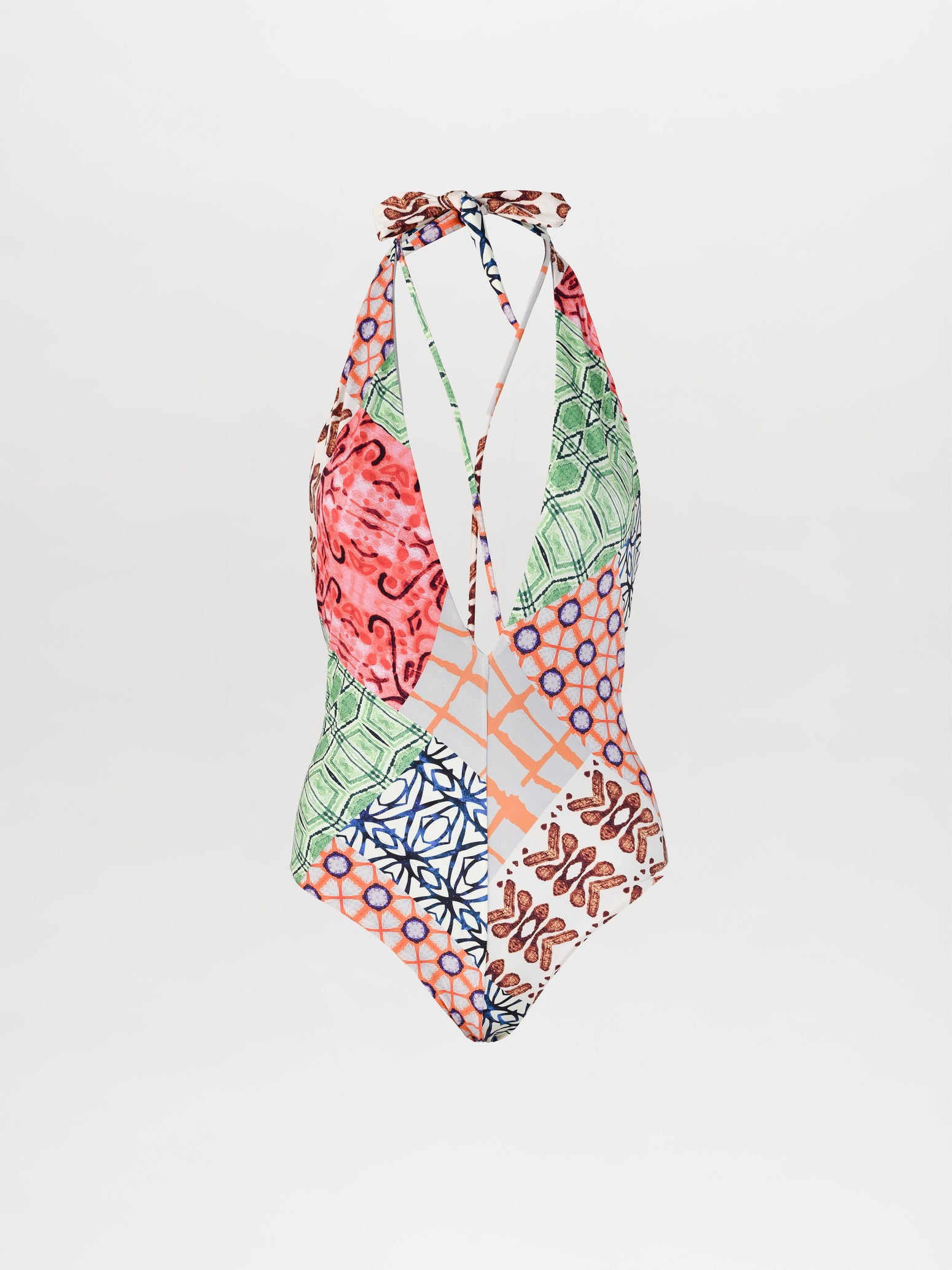 The Barthon Swimsuit by SilviaTcherassiEU is a halter-neck one-piece featuring bold geometric prints, a plunging neckline, and mixed floral patterns in shades of green, red, blue, and orange on a light background for a vibrant summer look.