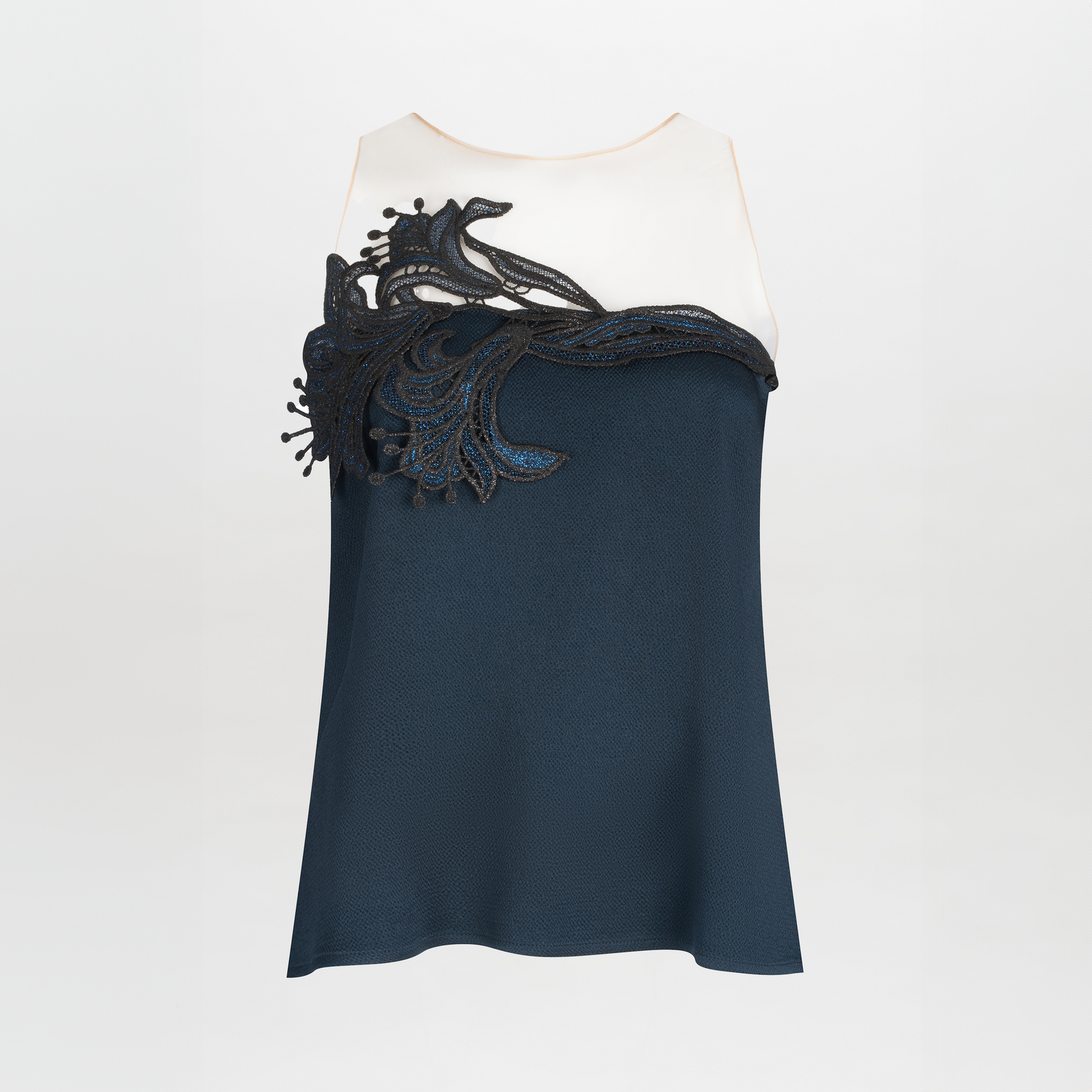 The Brisa Blouse by SVT DESIGNS features a sleeveless navy blue design with a white top section adorned in guipure lace. Decorative black lace on the upper front showcases floral or organic shapes against a plain light gray background.