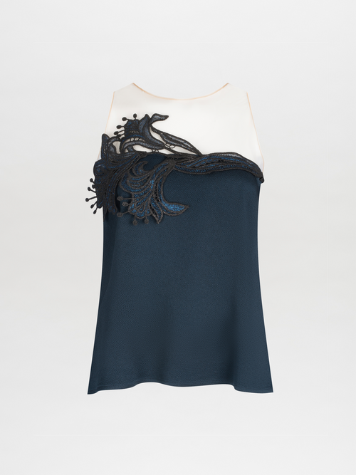 The Brisa Blouse by SVT DESIGNS features a sleeveless navy blue design with a white top section adorned in guipure lace. Decorative black lace on the upper front showcases floral or organic shapes against a plain light gray background.