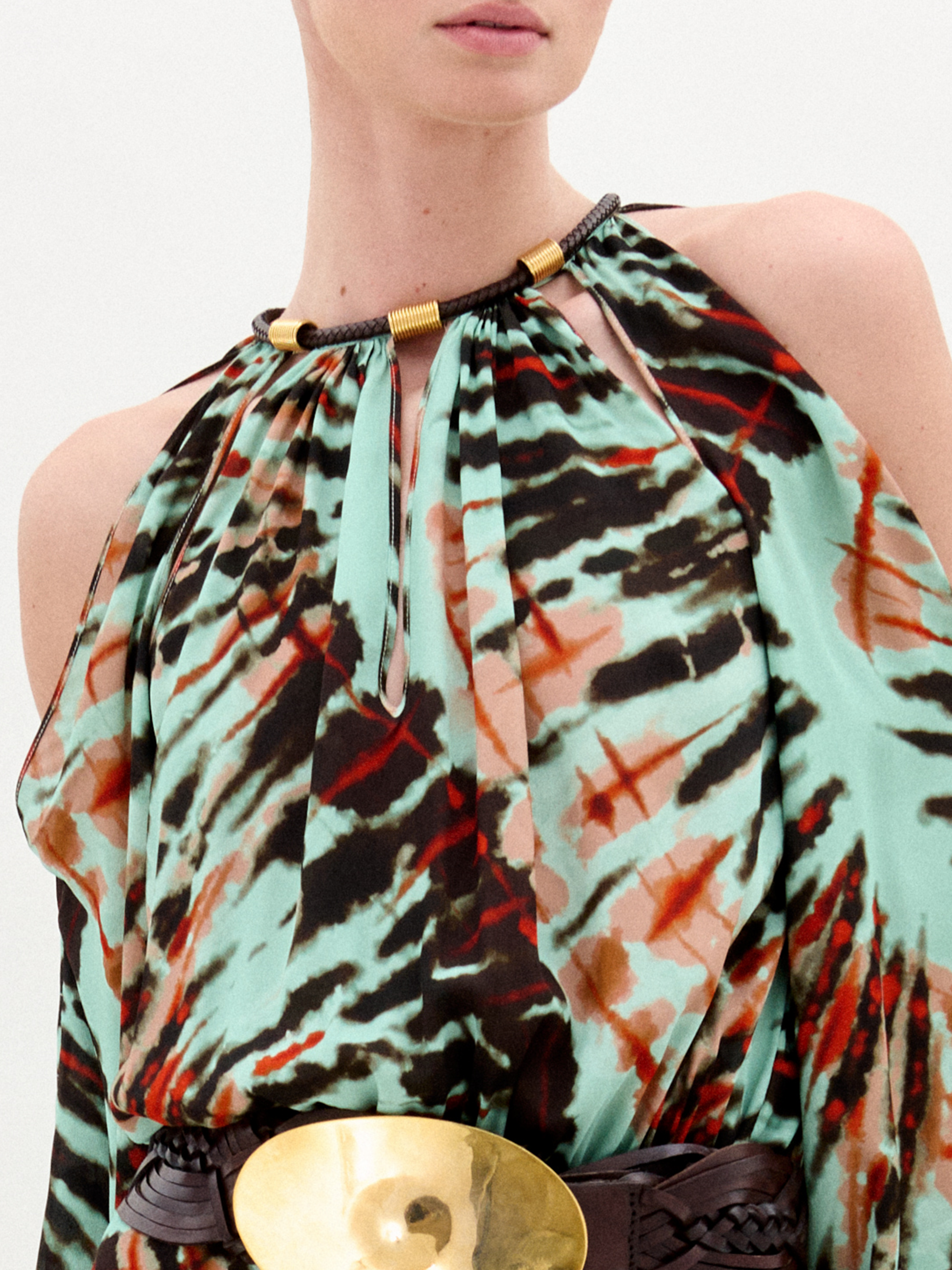 A woman wears the Carla Dress, a long patterned maxi with cut-out shoulders, a gathered neckline, long sleeves, a wide belt, and crafted from luxurious Italian fabric, standing against a plain white background.