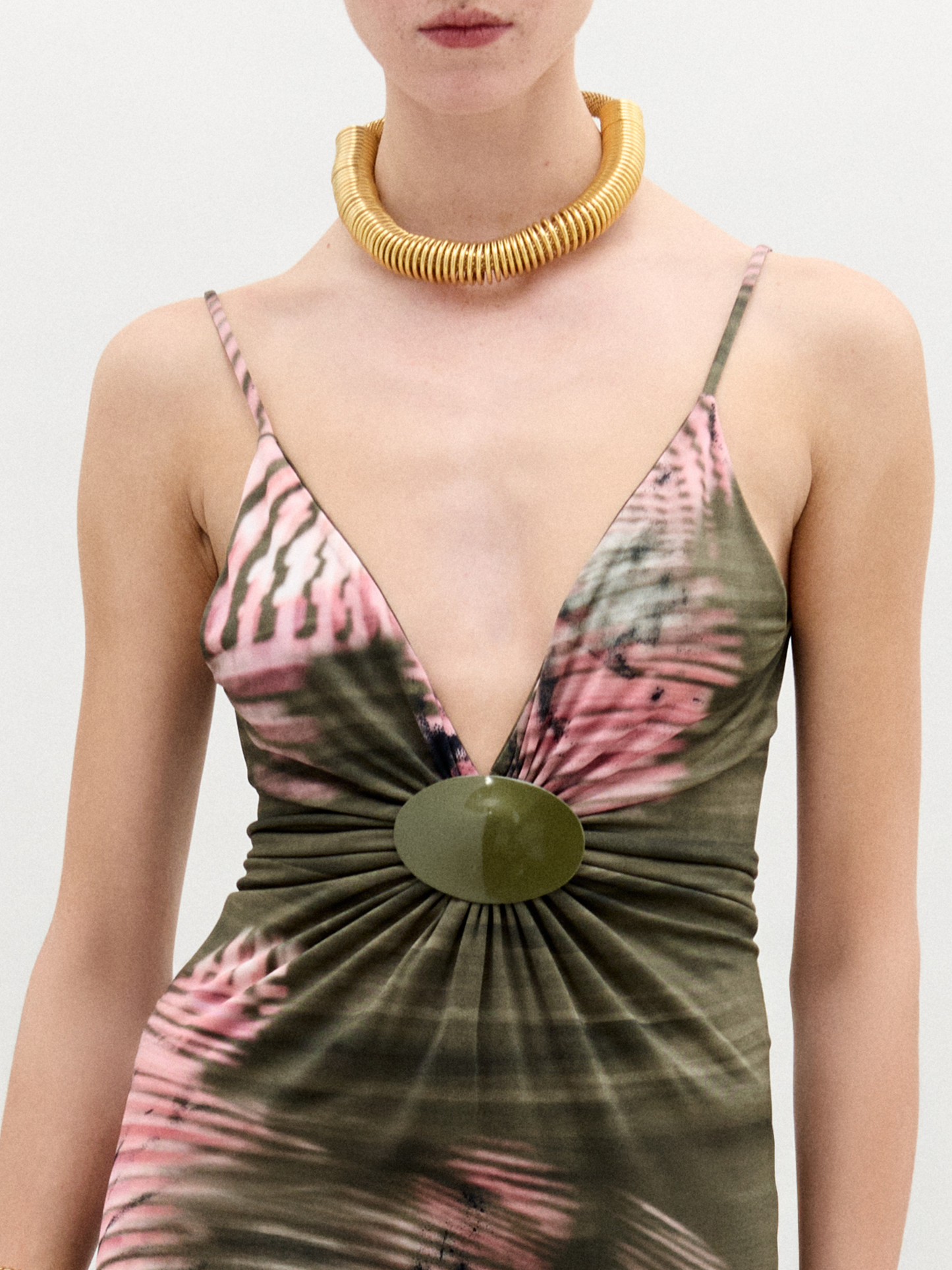 A woman poses against a plain background wearing the Carmin Dress— a floor-length, sleeveless maxi crafted from Italian fabric with a pink and olive green tie-dye pattern and a deep V neckline.