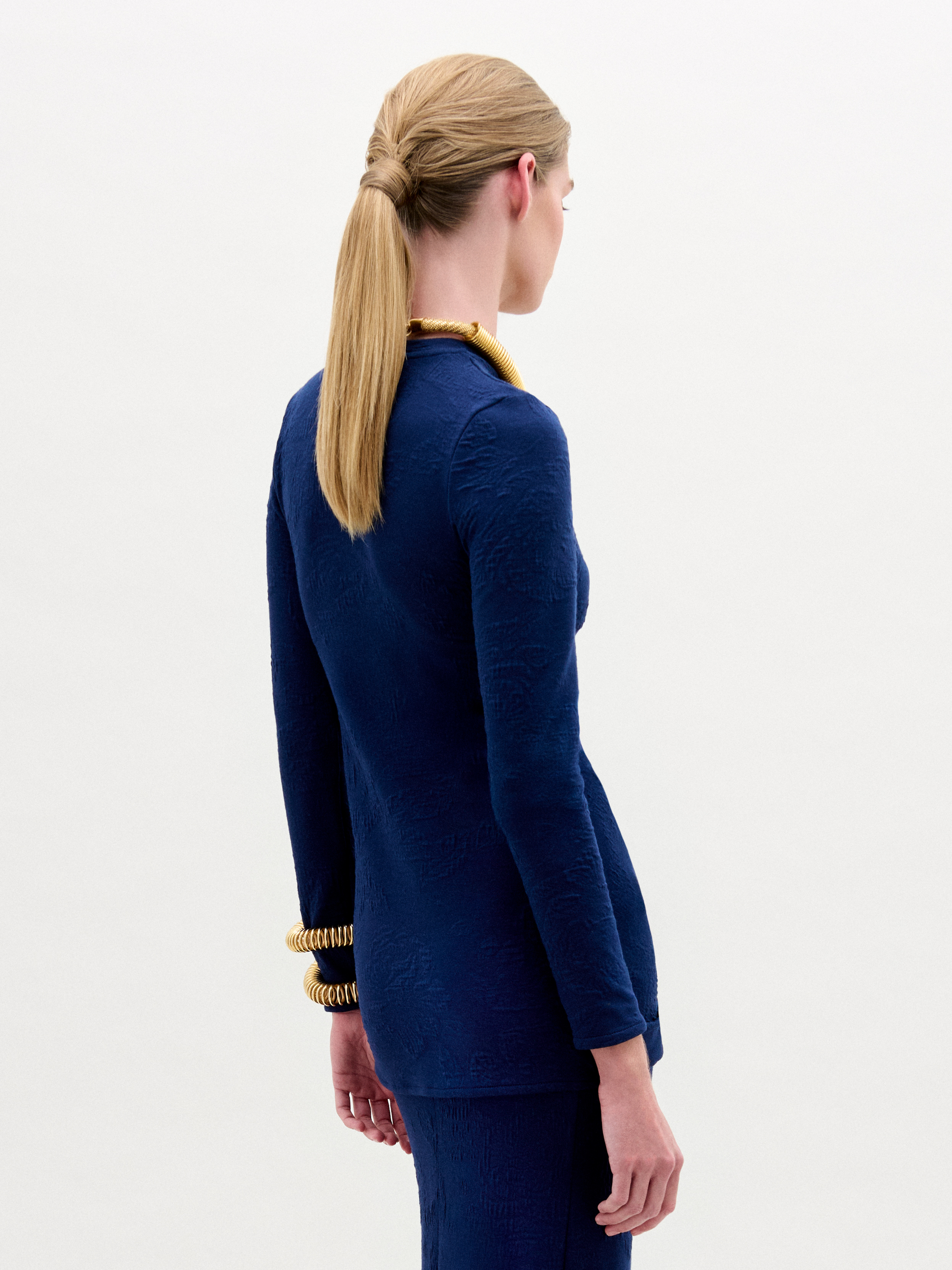 Woman wearing the Celyse Tshirt, a fitted long-sleeve navy top with front knot detail and a flattering silhouette, styled with gold jewelry against a plain white background.