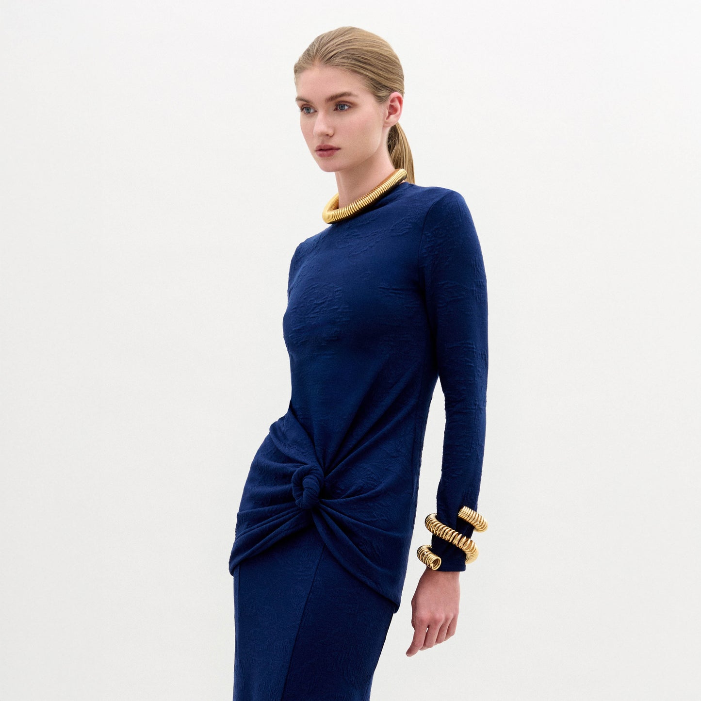 Woman wearing the Celyse Tshirt, a fitted long-sleeve navy top with front knot detail and a flattering silhouette, styled with gold jewelry against a plain white background.