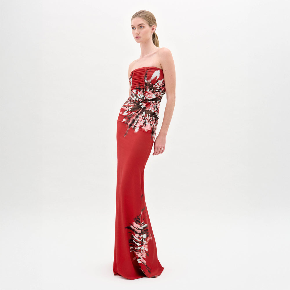A woman models the Collins Dress by SVT DESIGNS—a strapless maxi with a fitted bodice and abstract red, white, and black Italian print—set against a plain white background.