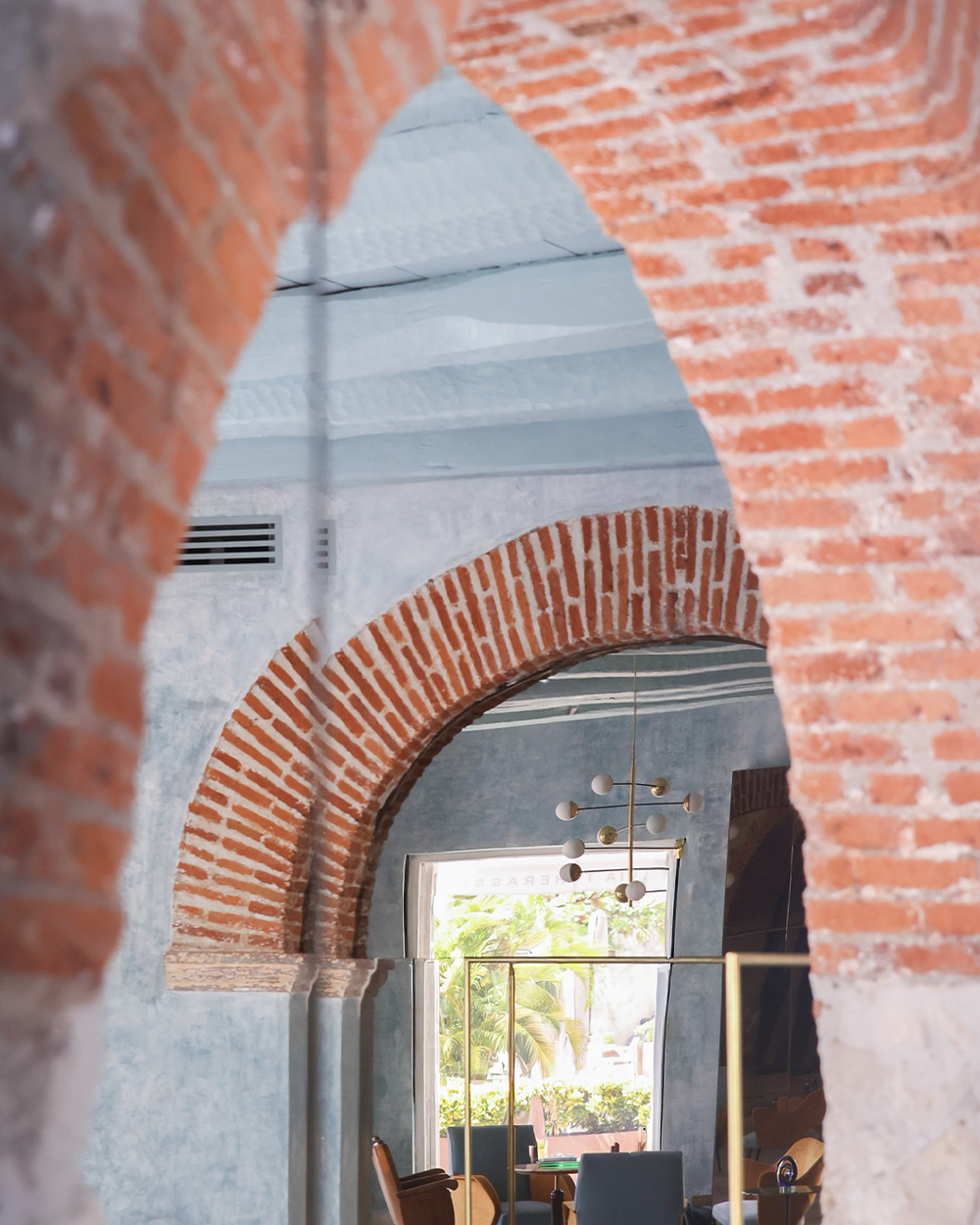 Archway with brick detailing leading to a modern interior with a chandelier.