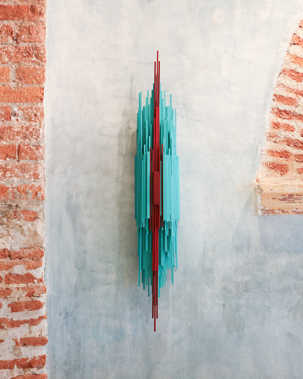 Modern wall sculpture with turquoise and red elements on a textured wall.