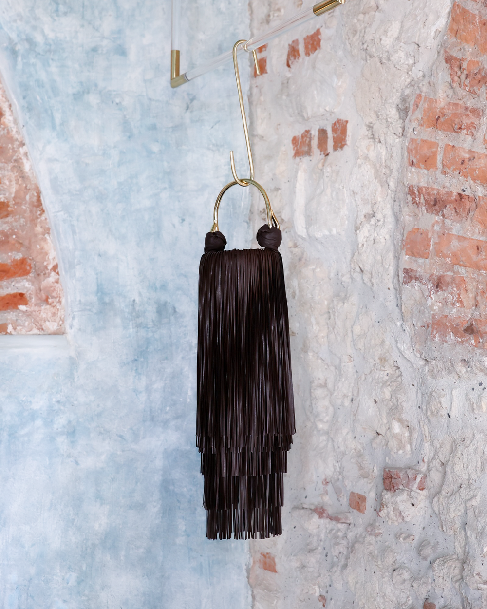 Black tassel earring hanging against a textured wall with brick accents